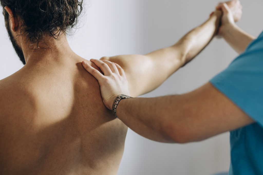 Physical Therapy: Chiropractor Doing Shoulder Adjustment While Patient Is Sitting On The Bed Centre Épaule Main Fribourg